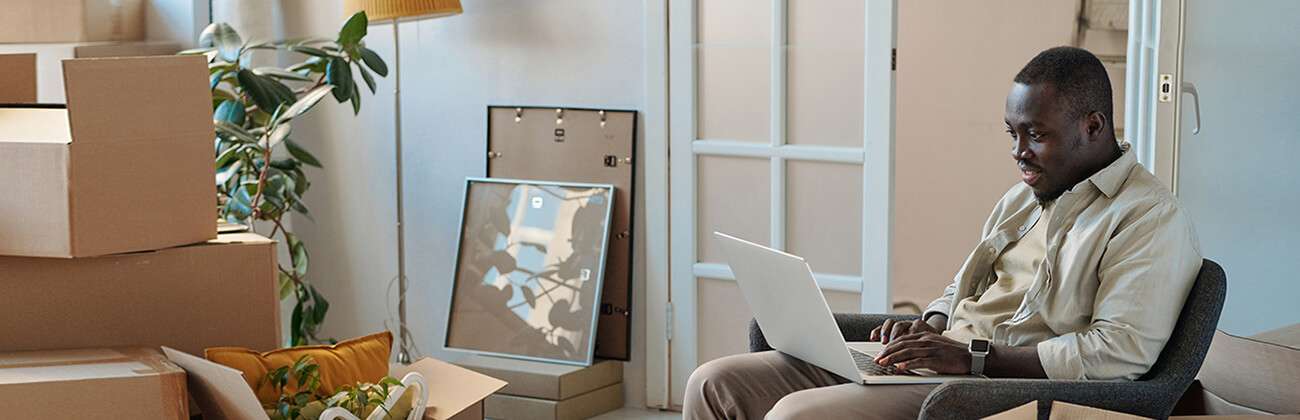 African American man on laptop surrounded by moving boxes uses the Astound moving checklist to set up his new internet service.