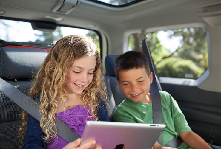 two kids in a car watching tv on their tablet